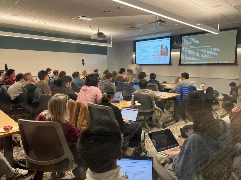 A room of researchers with laptops watching a presenter during an AlphaFold3 training session